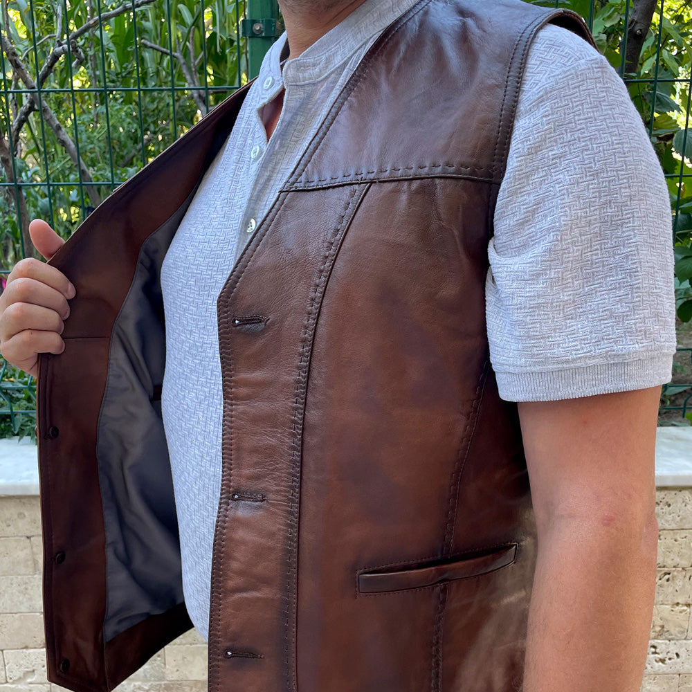 Close-up of a man standing outdoors, wearing a dark brown leather vest.